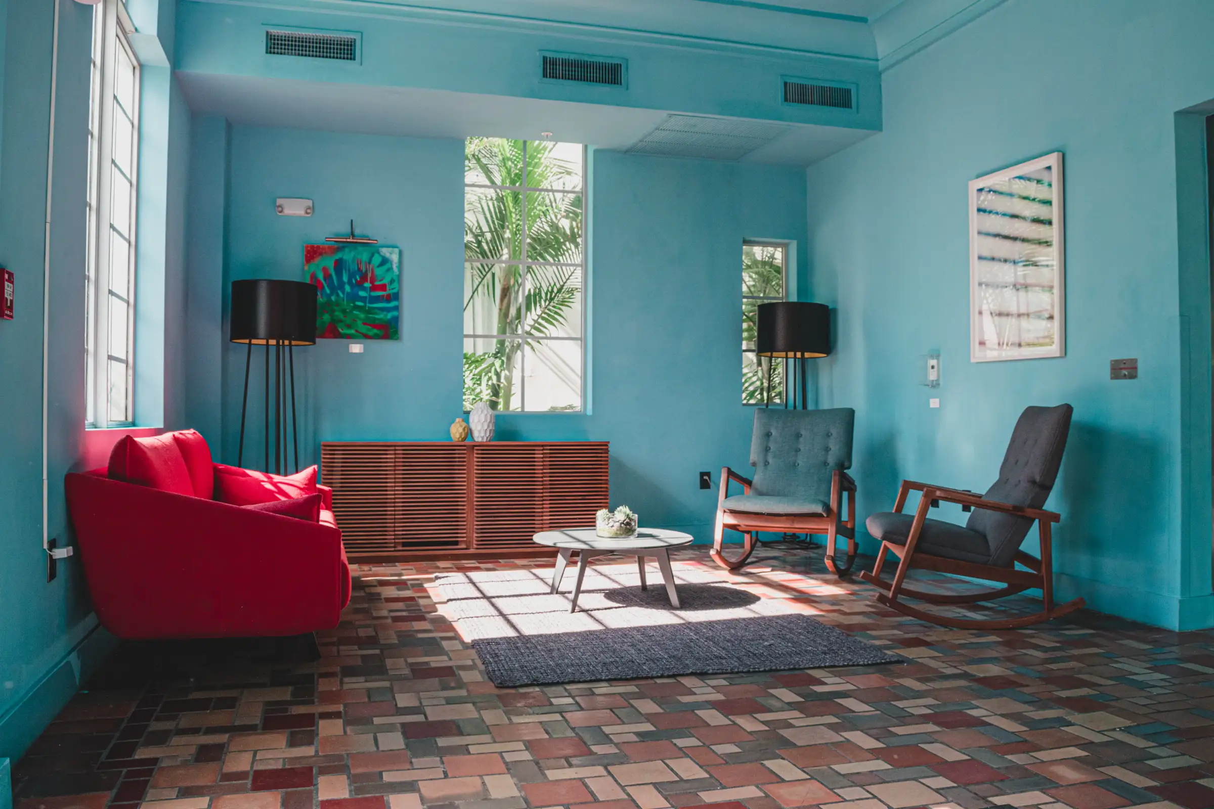 Heller Beratungsraum mit rotem Sofa, zwei Schaukelstühlen und einem Fenster zum Garten